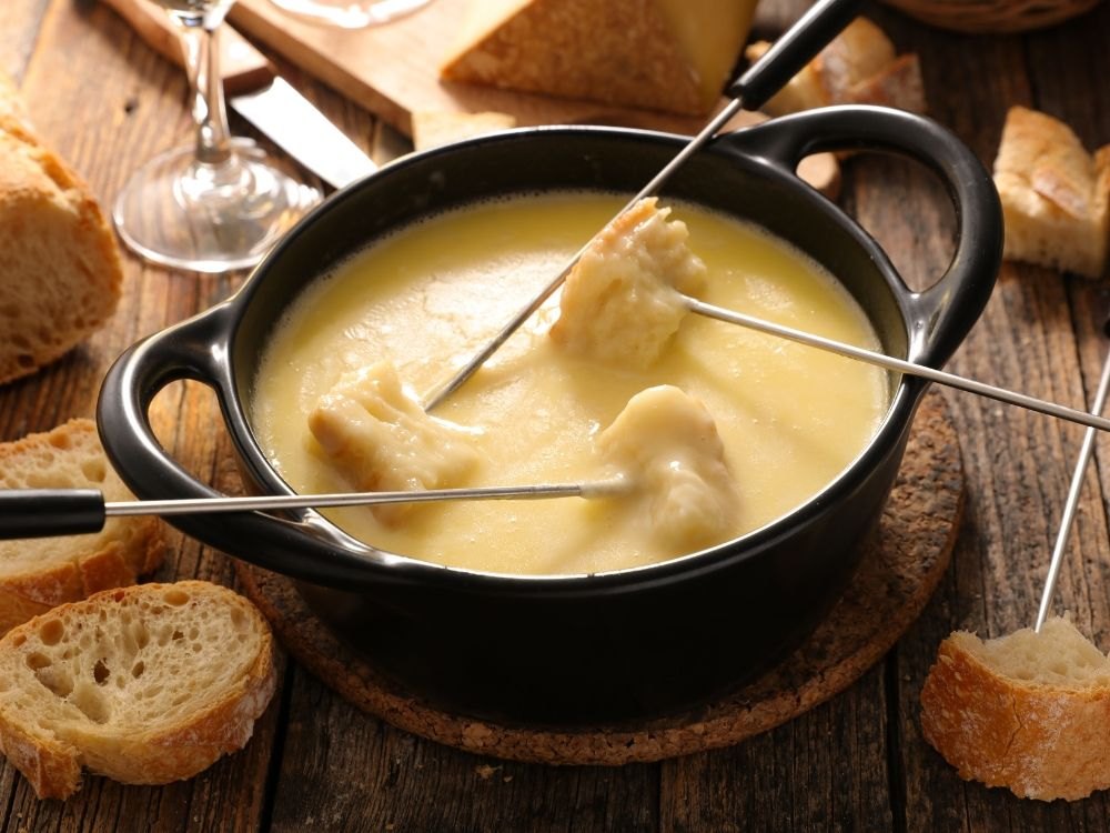 Käsefondue in einem schwarzen Topf, mit Baguettestücken auf Fonduegabeln